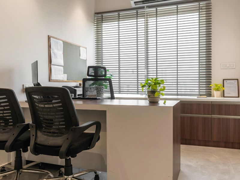 Moderna kancelarija sa ergonomskim stolicama sa lumbalnom podrškom, radnim stolom i prirodnim osvetljenjem kroz roletne.