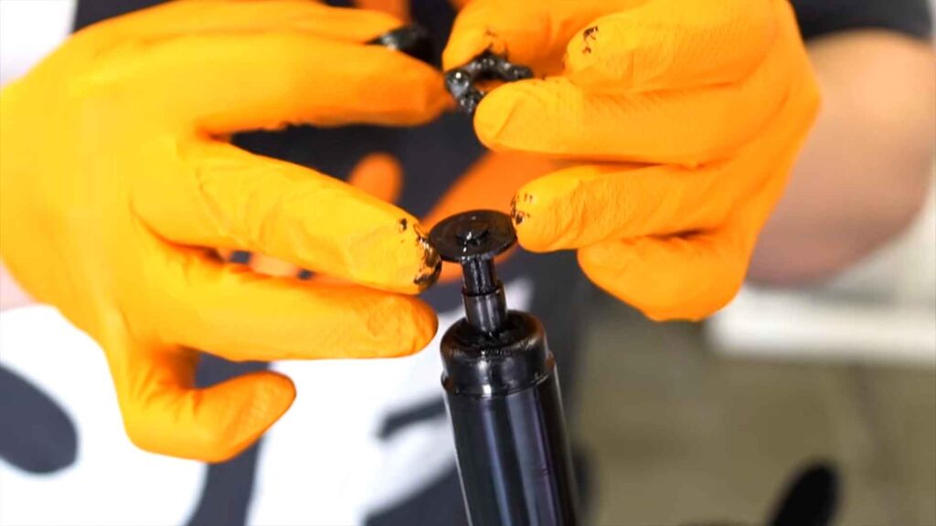 Ruke u narandžastim rukavicama postavljaju podmazani metalni deo na cilindar stolice