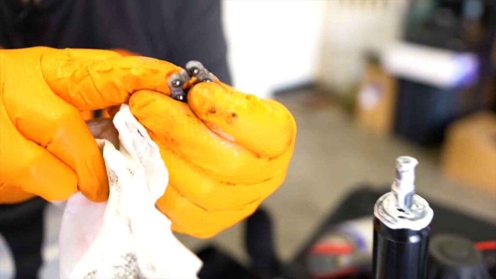 Ruke u narandžastim rukavicama drže male metalne kuglice i čiste ih ubrusom