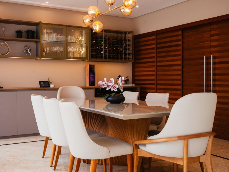 Bele stolice za trpezariju sa velikim stolom, dekorativnim svetlom u toploj atmosferi.