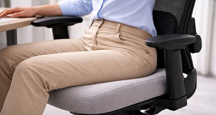 Osoba sedi u ergonomskoj stolici sa svetlosivim sedištem, prikaz krupnog plana sedišta i središnjeg dela, fokus na podršku i oblik.