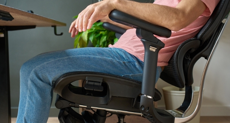 Osoba sedi u ergonomskoj kancelarijskoj stolici sa podesivim rukonaslonima.